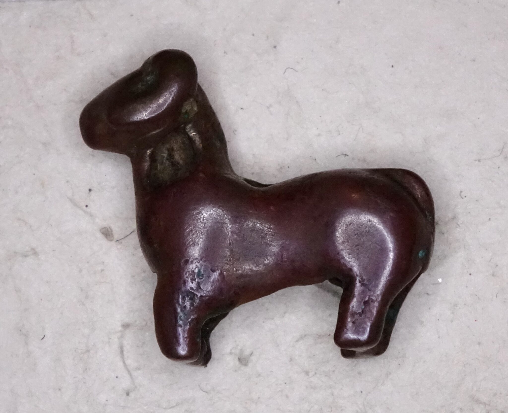 Smooth, purple-brown figurine of a sheep featuring curved horn, prominent musculature, and wooly neck
