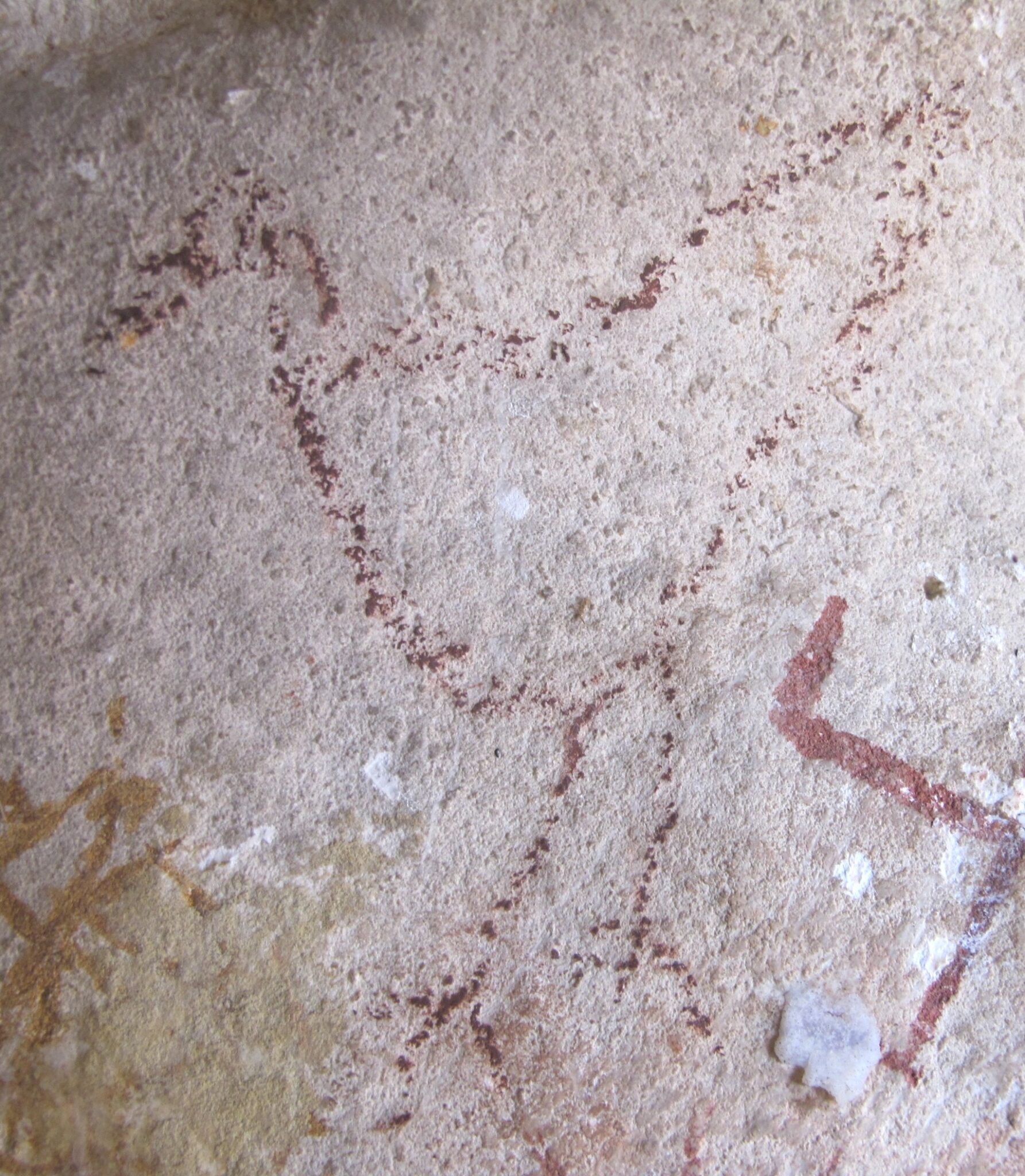 Form of a bird outlined in barely suggested rust-red pigment on rough white rock