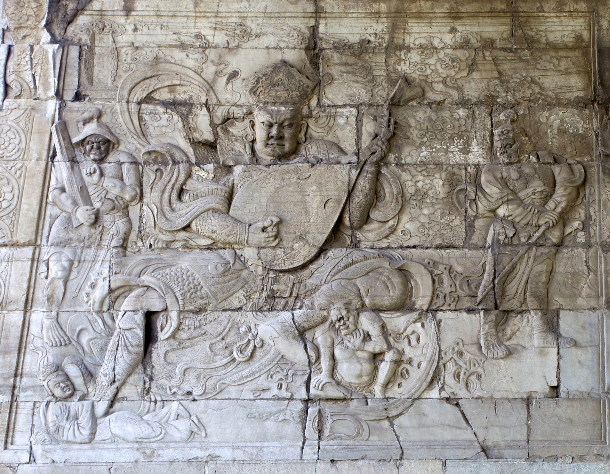 Relief on stone wall featuring dynamically posed central figure playing musical instrument; text panels at right