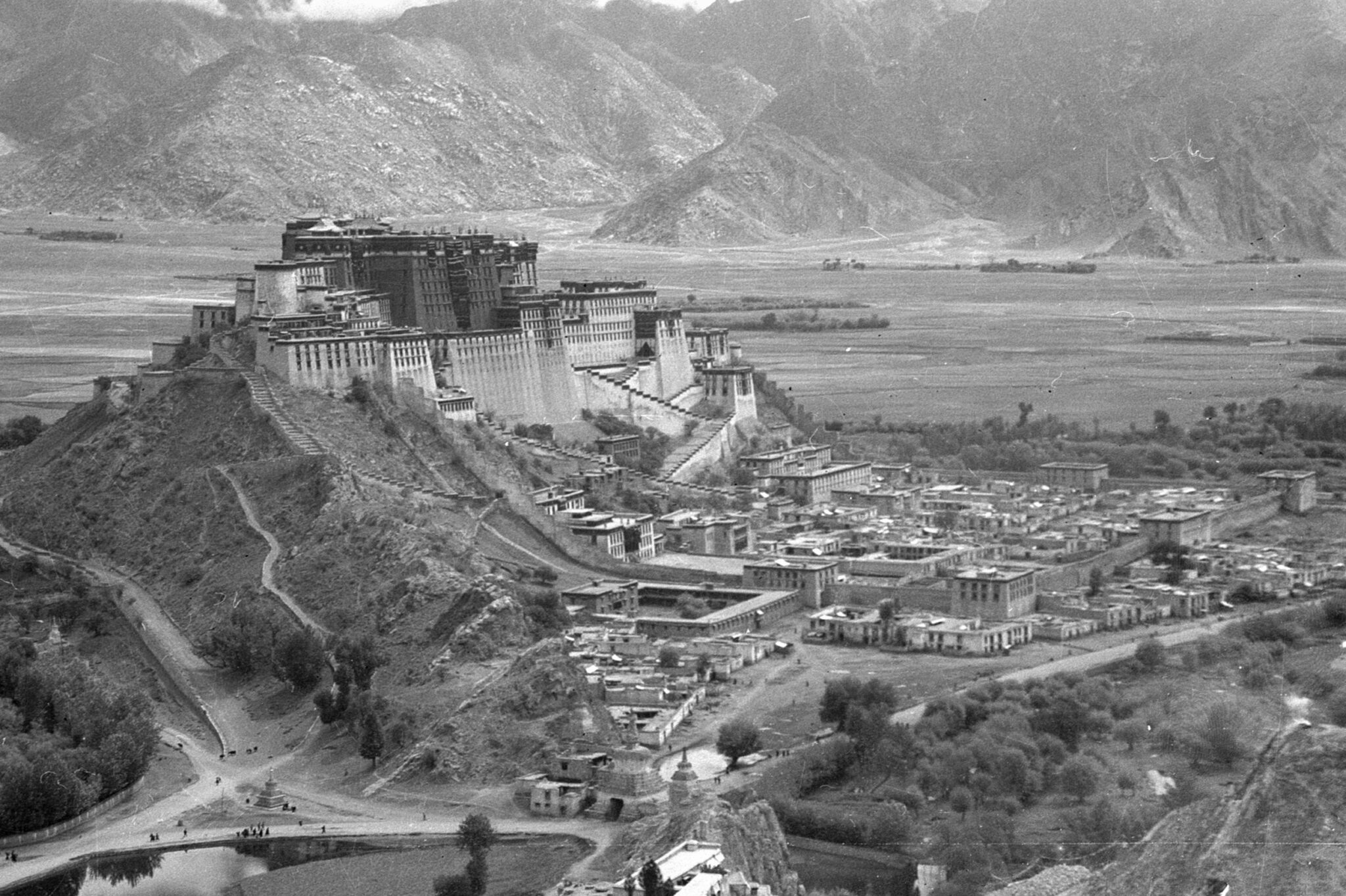 Black and white aerial photograph of palace complex situated on peak of hill within mountain valley