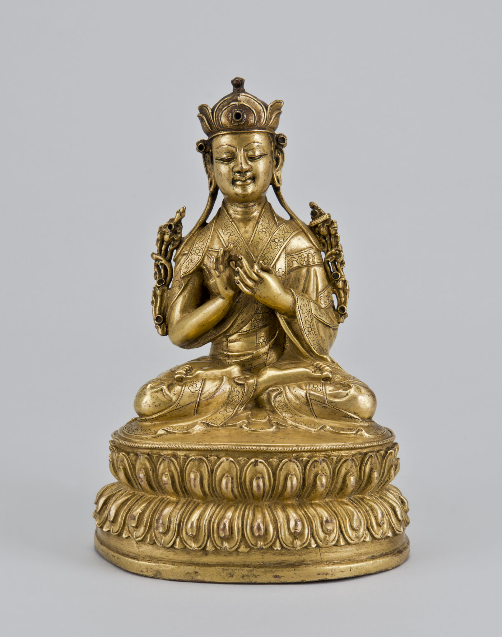 Golden statuette depicting lama seated on lotus pedestal with hands in mudras at chest