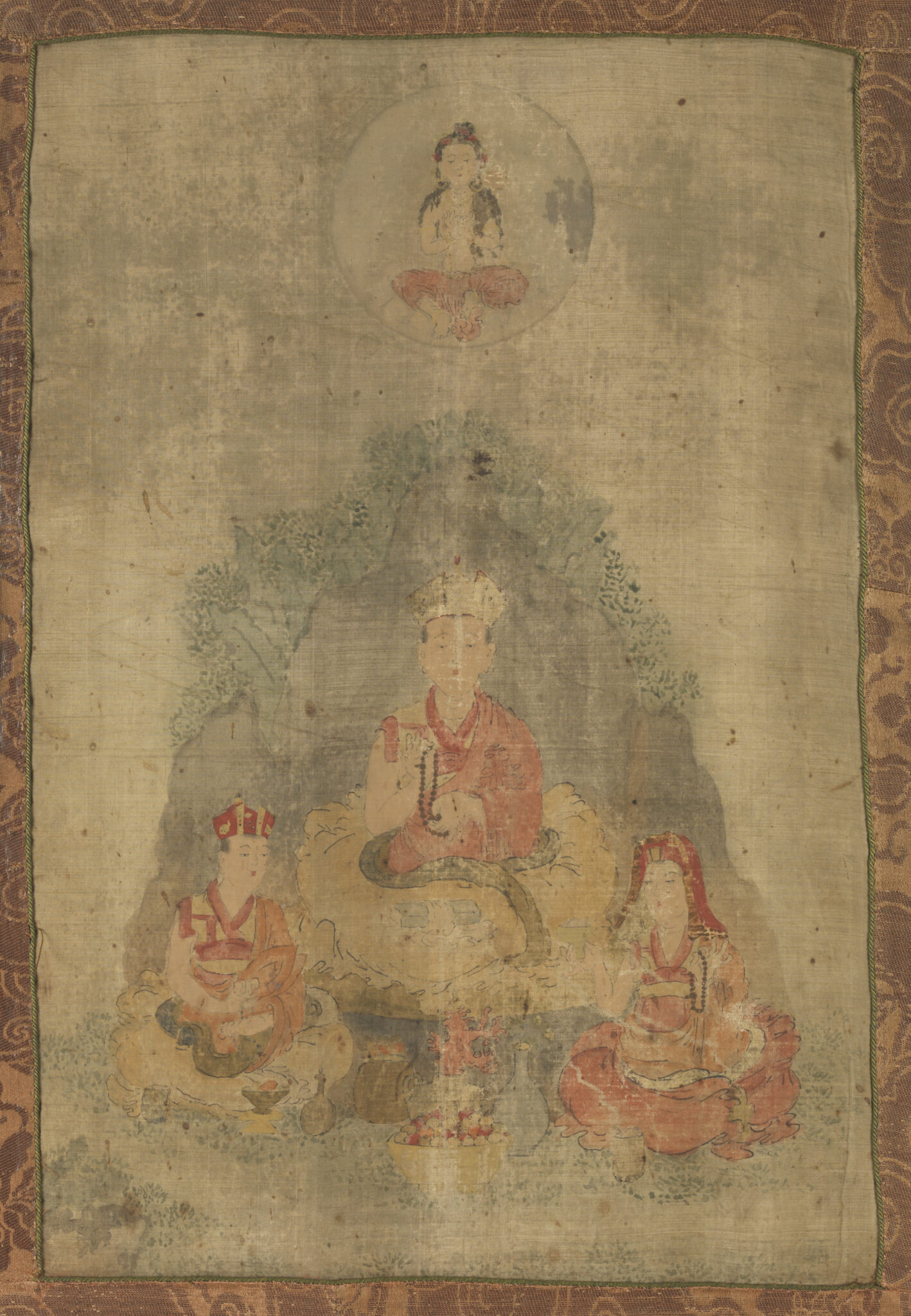 Painting mounted on brown damask depicting lama seated before rocky outcropping, flanked by attendants