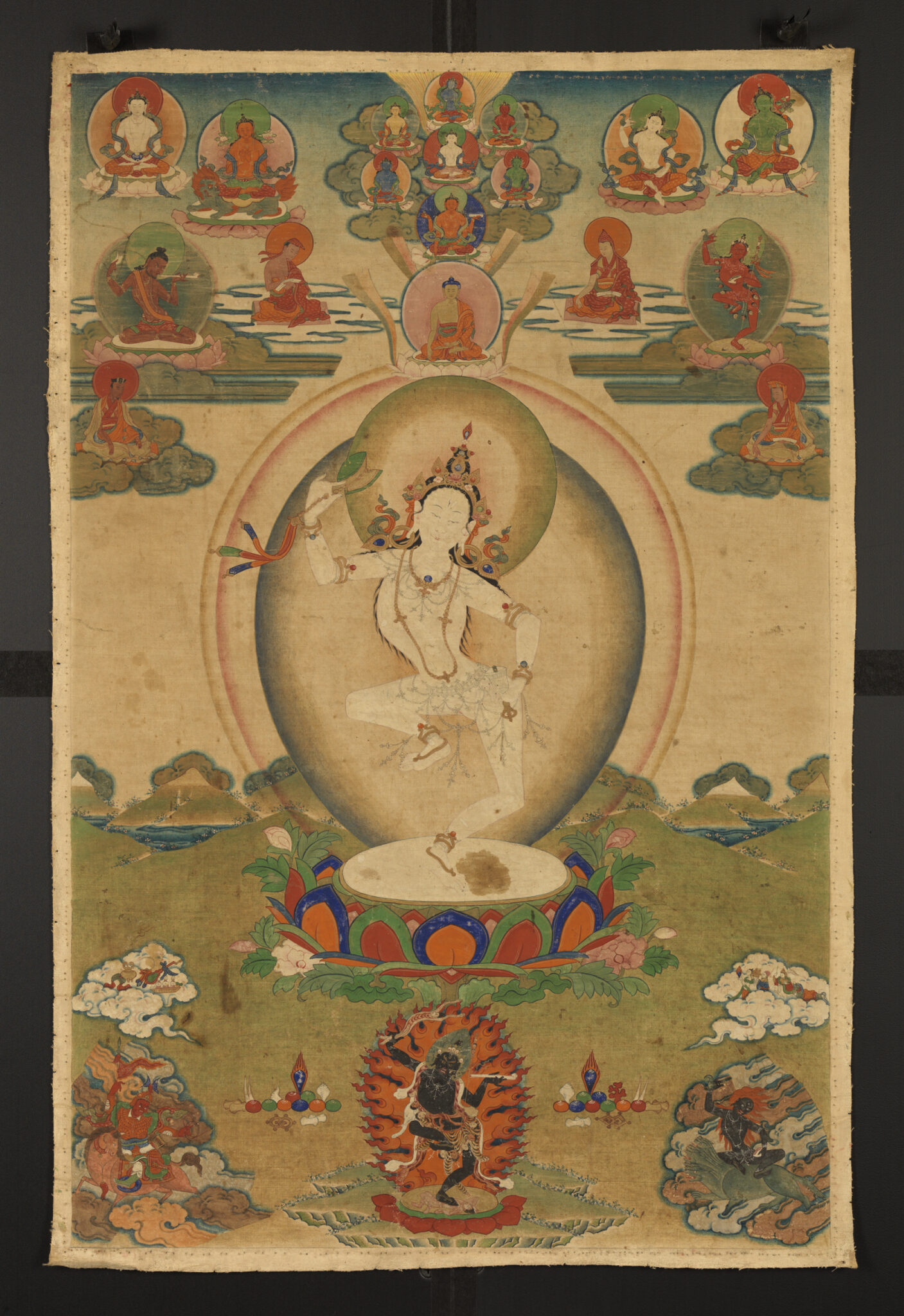 Deity dances upon lotus pedestal, beneath deity portraits, while raising drum in left hand