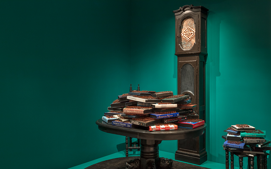 Nari Ward (b. 1963, St. Andrew, Jamaica; lives and works in New York); Breathing Room; 2019; used American history textbooks, stencil ink, French Country grandfather clock with African Fang figure, copper sheet with patina, copper nails, nesting table, narrow chair, lion's foot oval table, dome surveillance mirror, area rug; courtesy of the artist and Lehmann Maupin Gallery, New York, Hong Kong, and Seoul; installation photograph by David De Armas