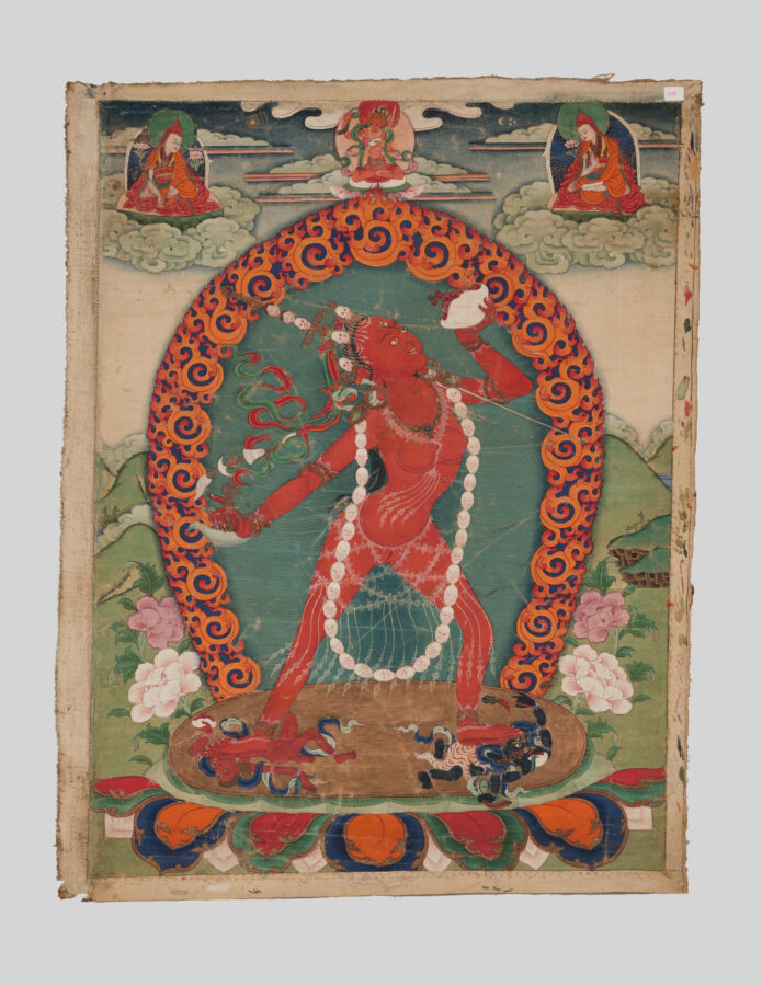 Thangka painting of a red goddess Vajrayogini wearing a bone garland, within a scrolling flame-patterned arch, flanked by lamas seated on clouds above and pink flowering plants below.