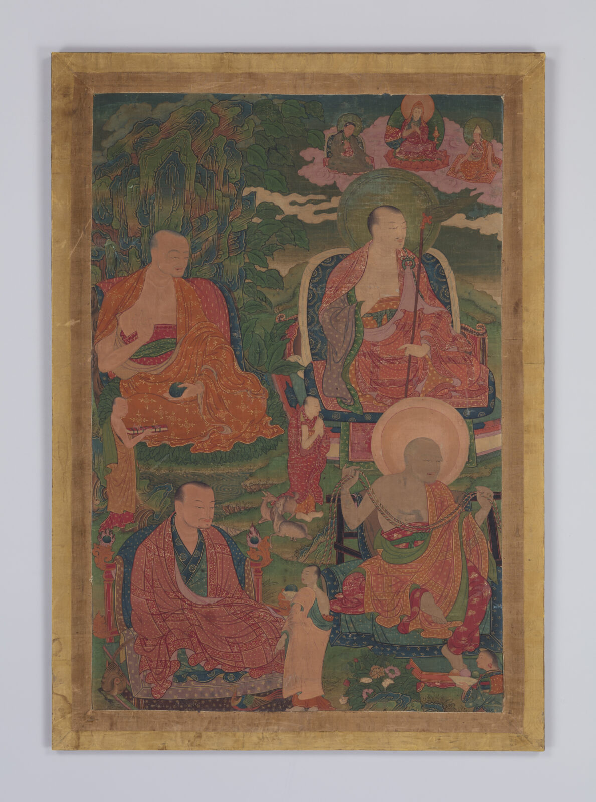 Thangka painting showing four seated Buddhist arhats in orange and red robes amid a green landscape, with a small figure at bottom center and three smaller deities seated on clouds in the upper right.