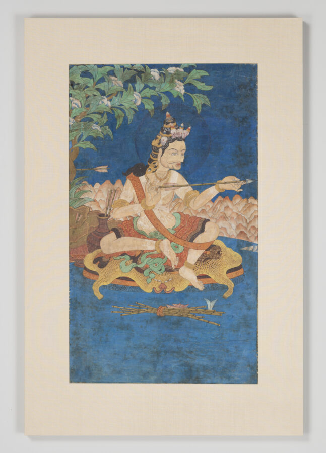 Painting of a crowned figure seated on a tiger skin holding an arrow, with a quiver beside him, under a flowering tree against a deep blue background with mountains and floating arrows below.
