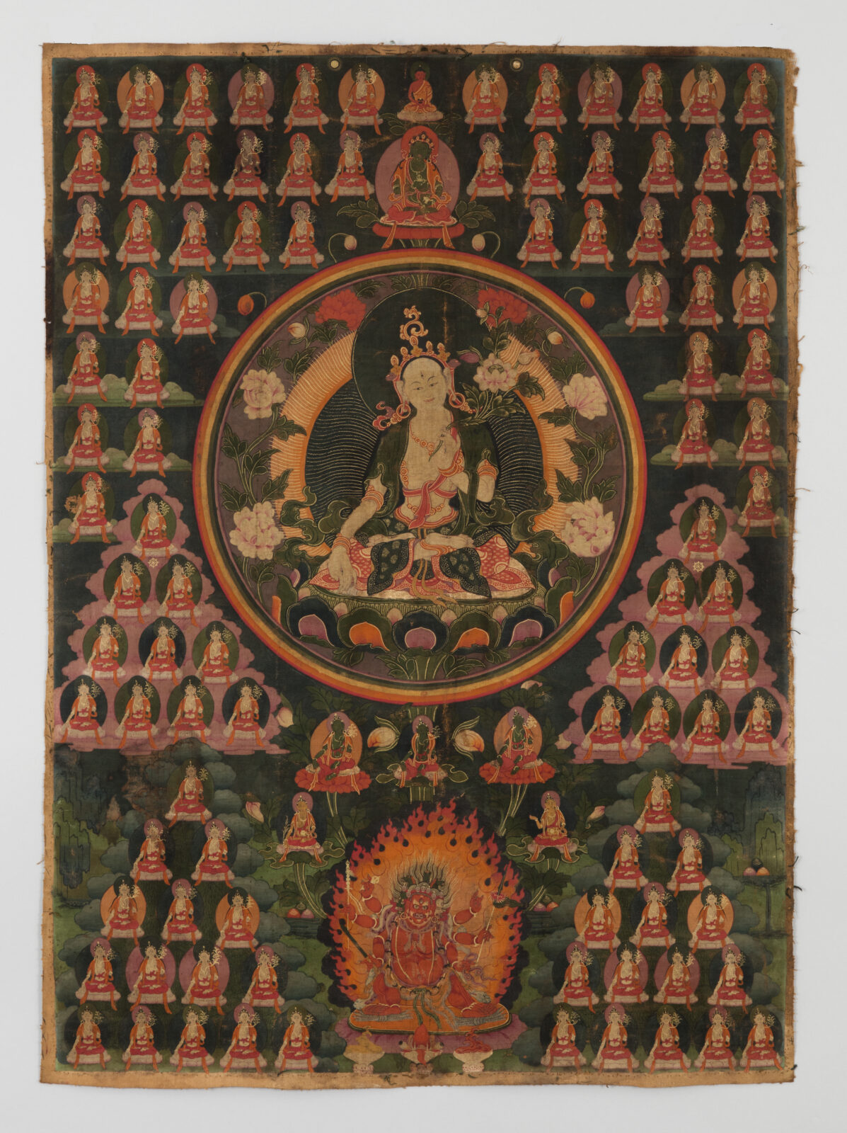 Thangka painting of a central crowned Buddhist deity in a circular halo, surrounded by many small rows of repeating, seated deities, with a flame-wreathed wrathful deity below.