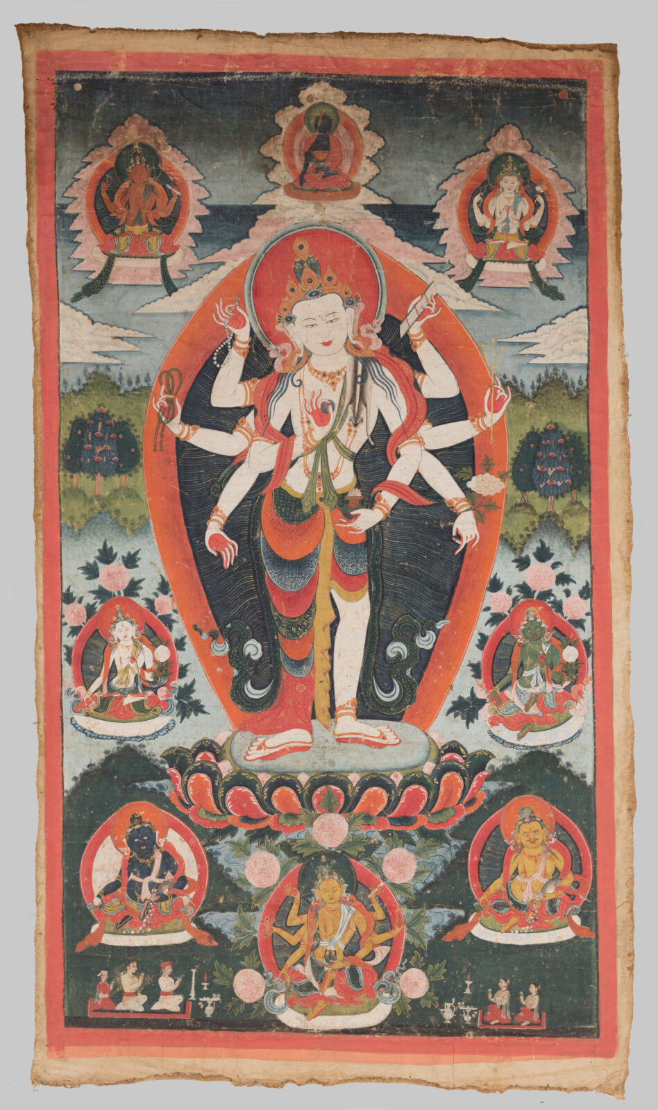 Thangka painting of a standing multi-armed deity with a crown and orange aureole, poised on a lotus base, surrounded by six smaller seated deities in framed roundels and a green landscape background.