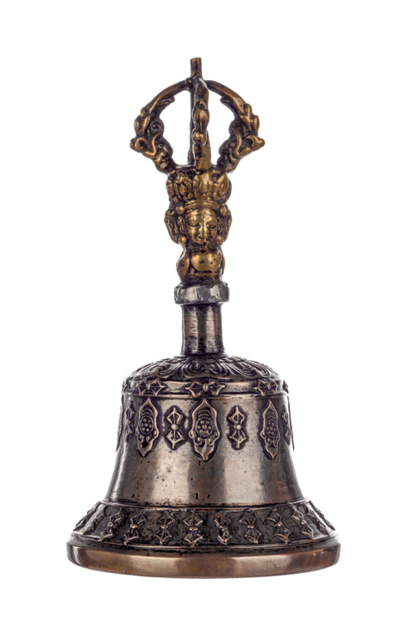 Metal bell with detailed engravings. The handle has a human head below a double-ended, symmetrical structure resembling four crescent moons that meet at the top.