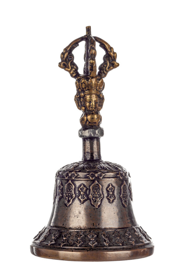 Metal bell with detailed engravings. The handle has a human head below a double-ended, symmetrical structure resembling four crescent moons that meet at the top.