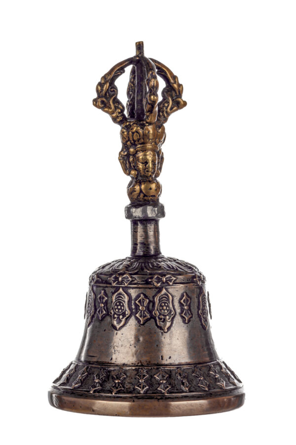 Metal bell with detailed engravings. The handle has a human head below a double-ended, symmetrical structure resembling four crescent moons that meet at the top.