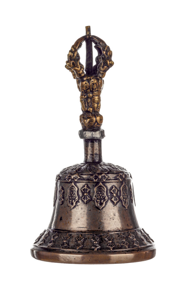 Metal bell with detailed engravings. The handle has a human head below a double-ended, symmetrical structure resembling four crescent moons that meet at the top.