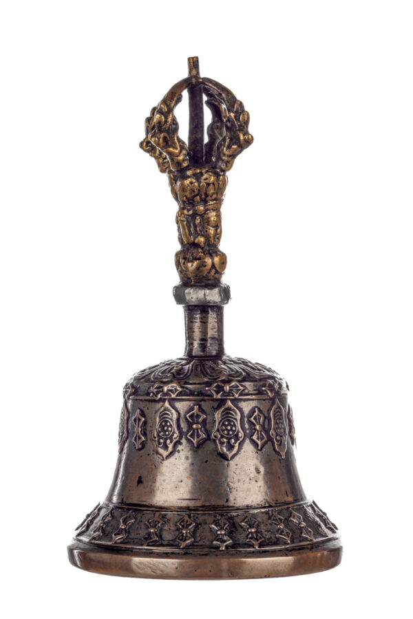 Metal bell with detailed engravings. The handle has a human head below a double-ended, symmetrical structure resembling four crescent moons that meet at the top.