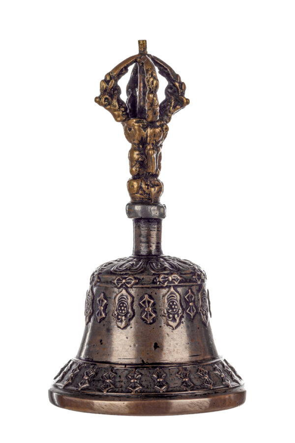 Metal bell with detailed engravings. The handle has a human head below a double-ended, symmetrical structure resembling four crescent moons that meet at the top.