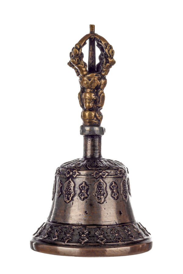 Metal bell with detailed engravings. The handle has a human head below a double-ended, symmetrical structure resembling four crescent moons that meet at the top.