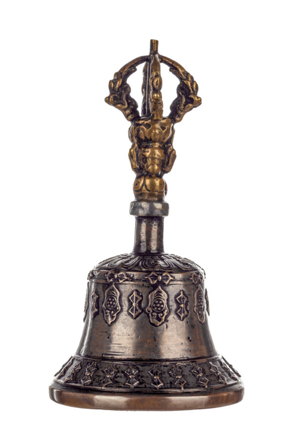 Metal bell with detailed engravings. The handle has a human head below a double-ended, symmetrical structure resembling four crescent moons that meet at the top.