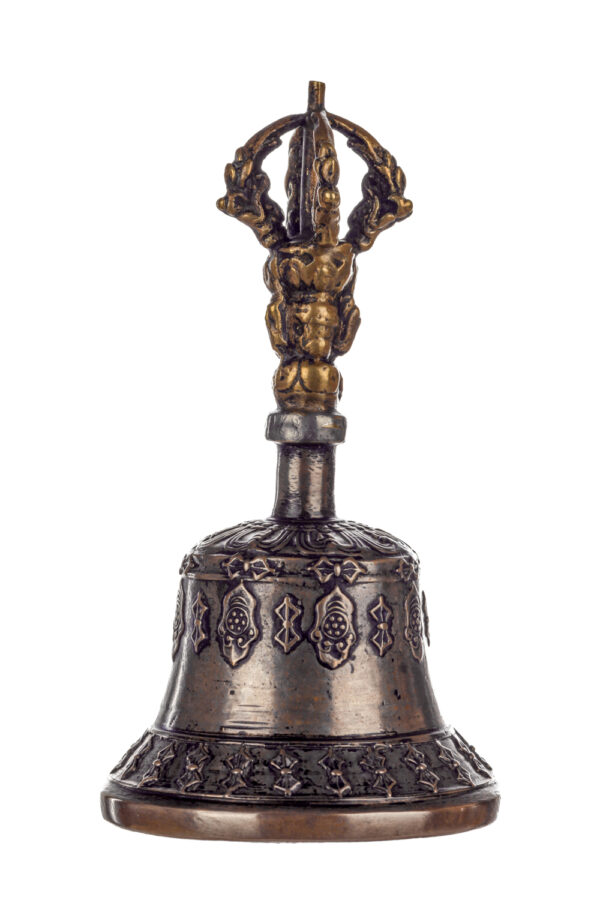 Metal bell with detailed engravings. The handle has a human head below a double-ended, symmetrical structure resembling four crescent moons that meet at the top.