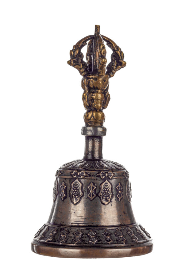 Metal bell with detailed engravings. The handle has a human head below a double-ended, symmetrical structure resembling four crescent moons that meet at the top.