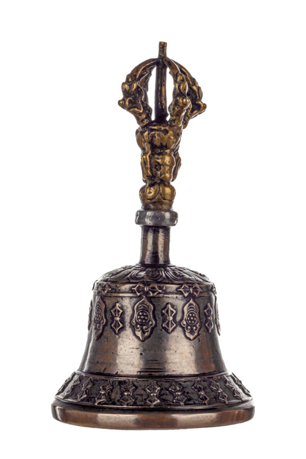 Metal bell with detailed engravings. The handle has a human head below a double-ended, symmetrical structure resembling four crescent moons that meet at the top.