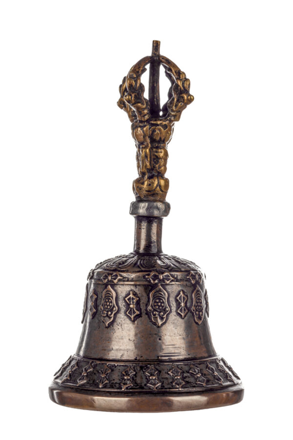 Metal bell with detailed engravings. The handle has a human head below a double-ended, symmetrical structure resembling four crescent moons that meet at the top.