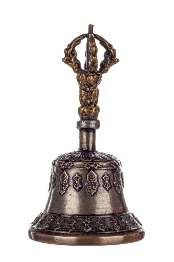 Metal bell with detailed engravings. The handle has a human head below a double-ended, symmetrical structure resembling four crescent moons that meet at the top.