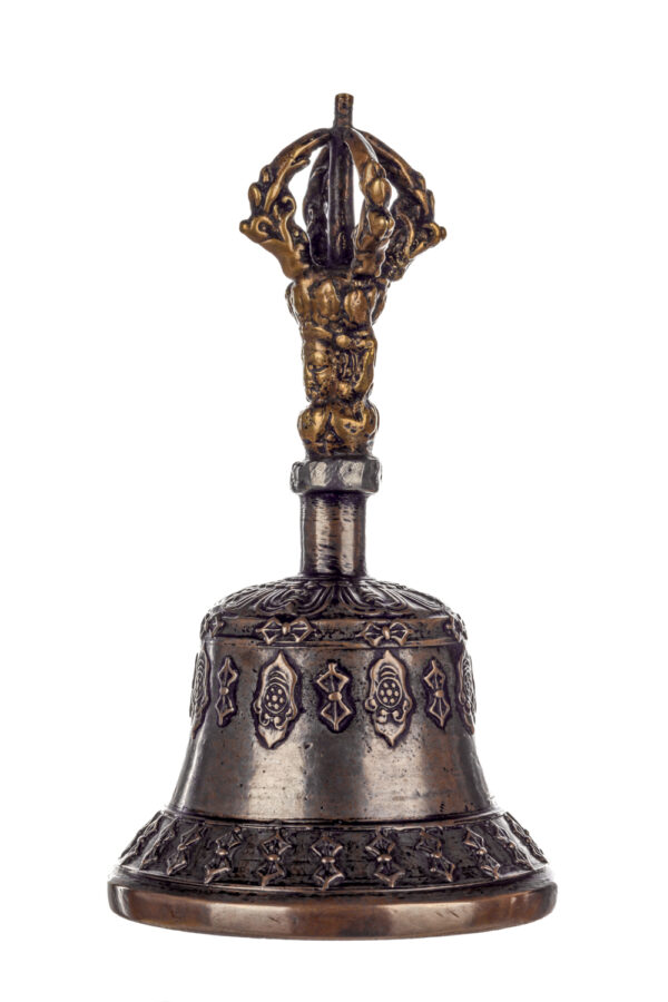 Metal bell with detailed engravings. The handle has a human head below a double-ended, symmetrical structure resembling four crescent moons that meet at the top.