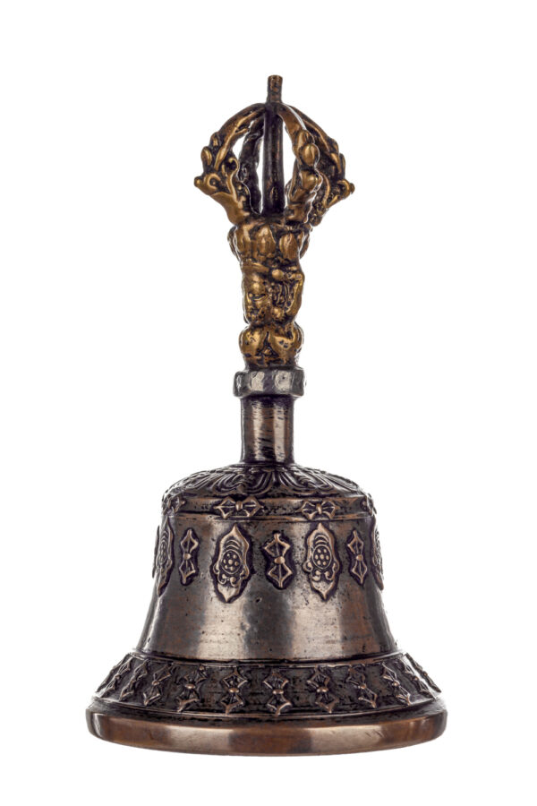 Metal bell with detailed engravings. The handle has a human head below a double-ended, symmetrical structure resembling four crescent moons that meet at the top.