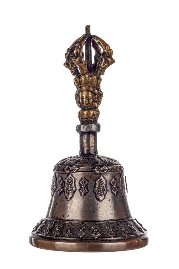 Metal bell with detailed engravings. The handle has a human head below a double-ended, symmetrical structure resembling four crescent moons that meet at the top.