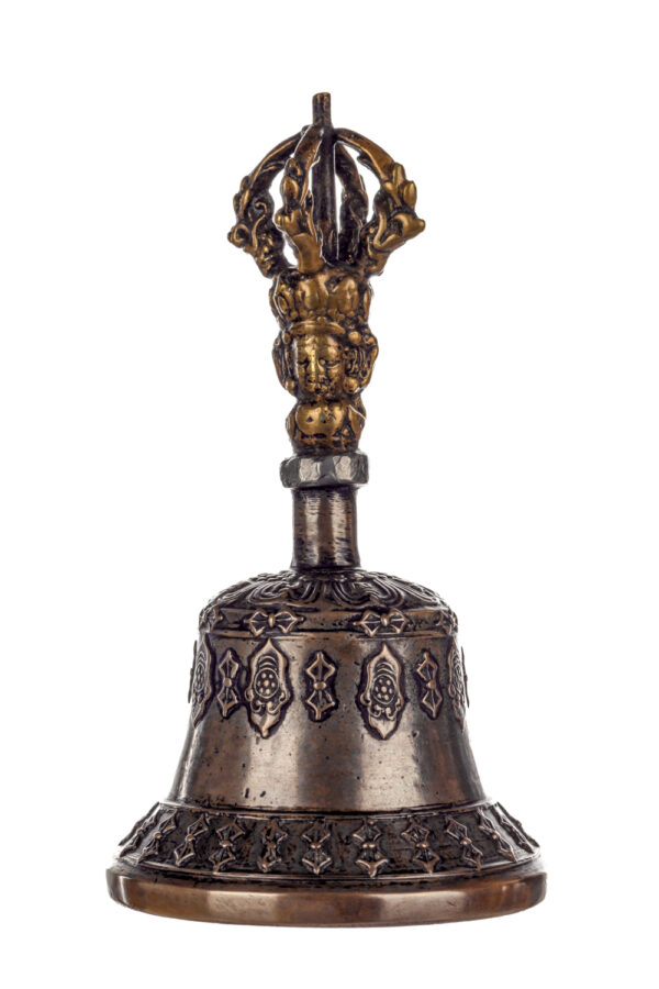 Metal bell with detailed engravings. The handle has a human head below a double-ended, symmetrical structure resembling four crescent moons that meet at the top.