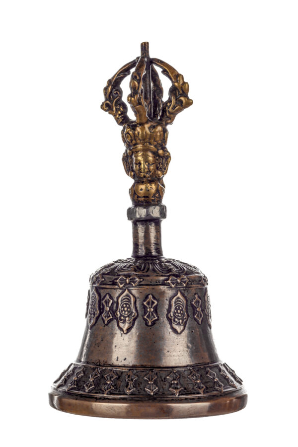 Metal bell with detailed engravings. The handle has a human head below a double-ended, symmetrical structure resembling four crescent moons that meet at the top.