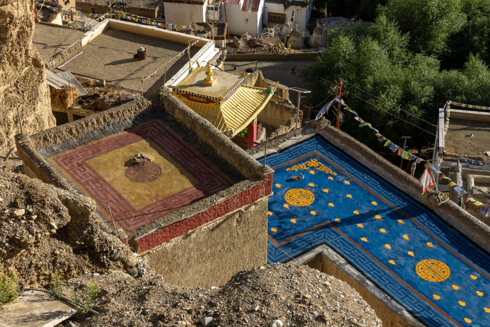 Overhead view of two rooftops in Ladakh, India, decorated with patterns resembling rugs, one red and yellow and the other blue and yellow