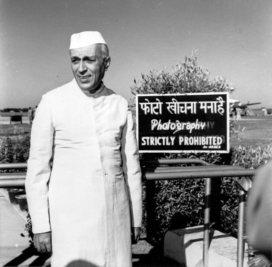 A black and white photograph of a man dressed in white standing in front of a strictly prohibited sign