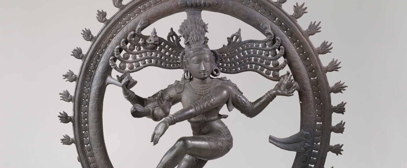 Metal statue of multi-armed figure surrounded by circle with flames.