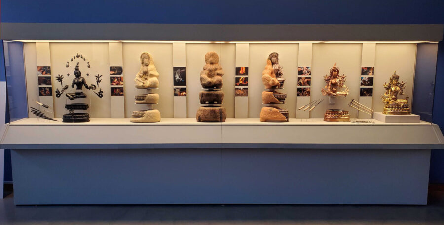 Glass vitrine displaying Buddhist sculptures and photographs.