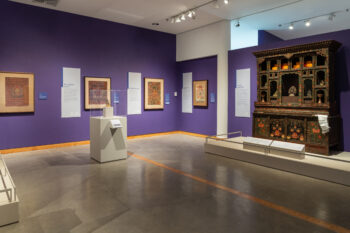 A photograph of an exhibition hall with wall text and artifacts displayed on the walls and pedestals