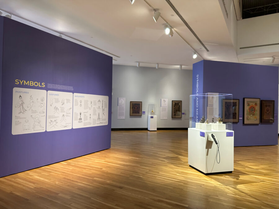 A photograph of an exhibition hall with wall text and artworks on the walls and pedestals