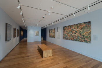 A photograph of an exhibition hall with artworks on the walls and a seating area in the center at the McMullen Museum of Art