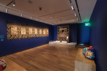 A photograph of an exhibition hall with artworks on the walls and short pedestals at the McMullen Museum of Art in Boston