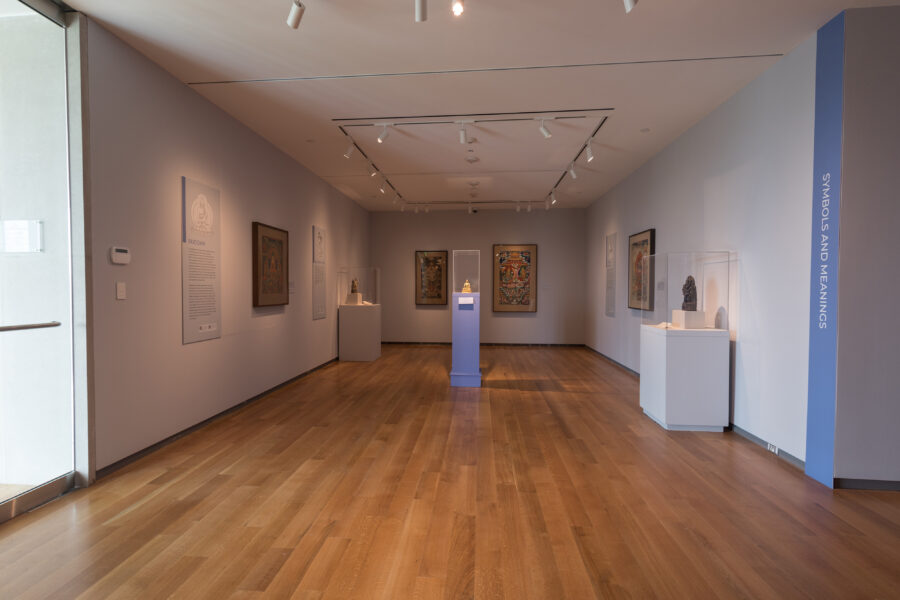 A photograph of an exhibition hall with artworks on the walls and pedestals at the McMullen Museum of Art in Boston