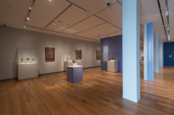 A photograph of an exhibition hall with artworks on the walls and pedestals at the McMullen Museum of Art