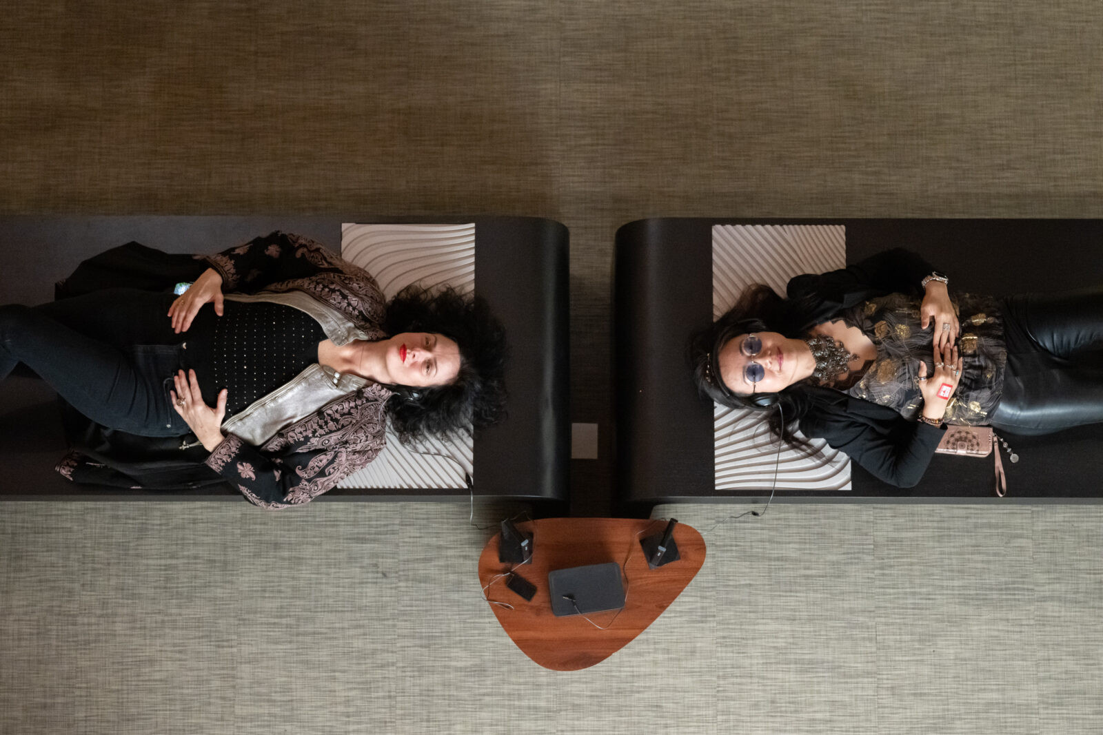 Overhead view of two adults with headphones lying on black benches.