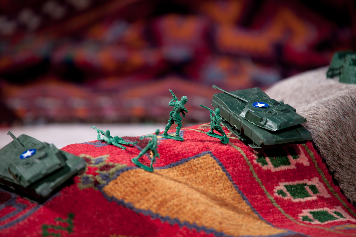 Small green plastic army figures and tanks perched on colorful tapestry.