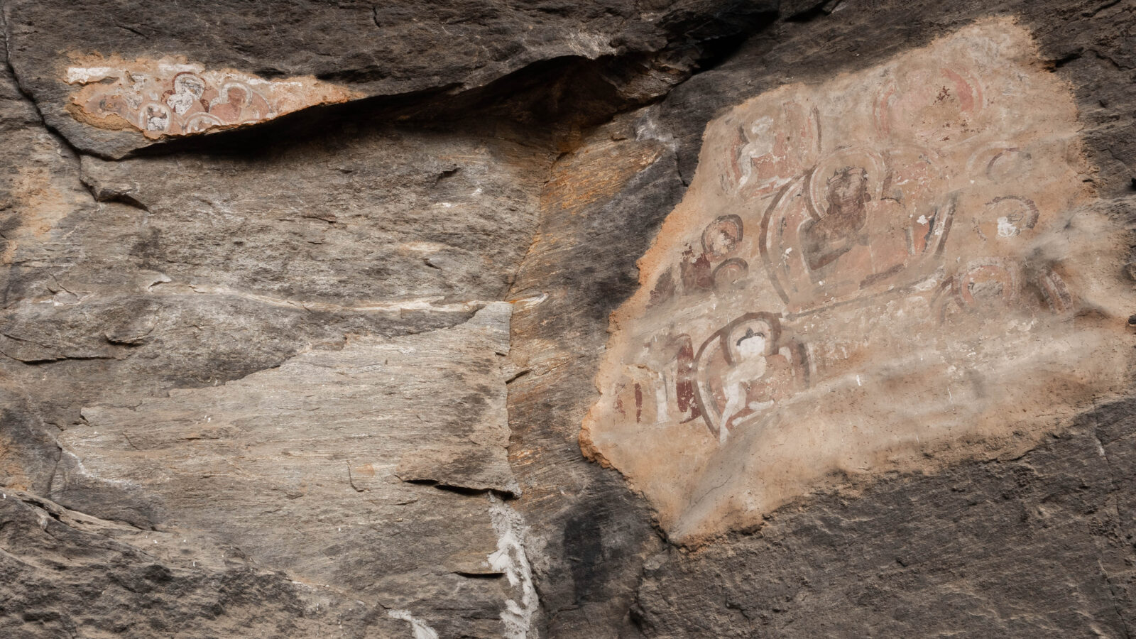 Faded figures painted in red, brown, and white on a rock wall