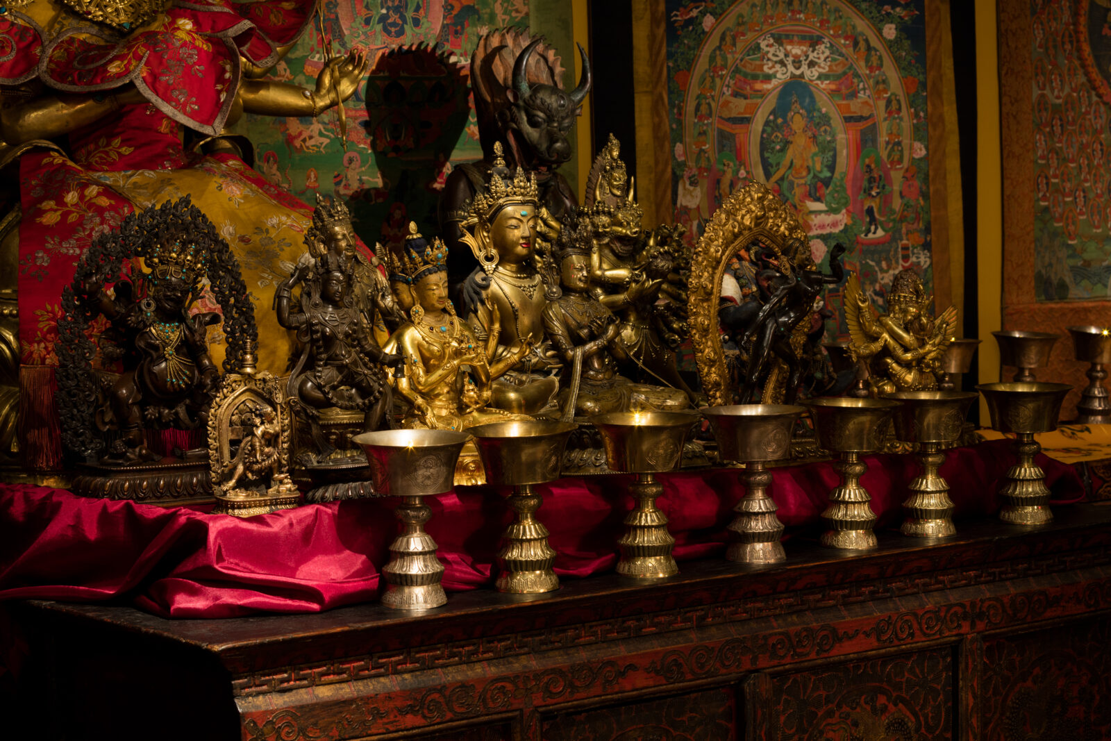 butter lamps and sculptures sit on top of a cabinet in the tibetan buddhist shrine room installation