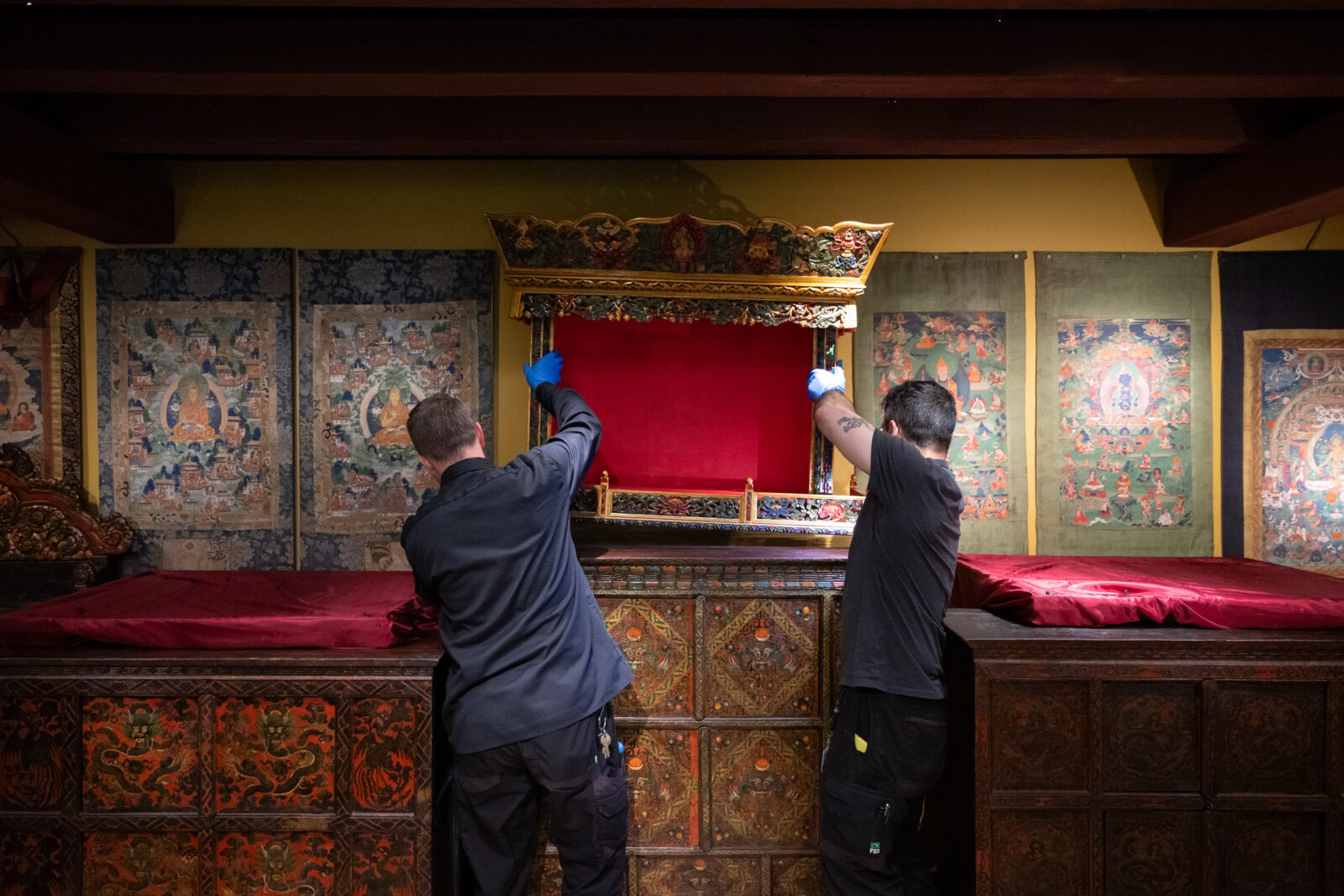 two art handlers lift a shrine room cabinet into place in the Rubin Museum Tibetan Buddhist Shrine Room