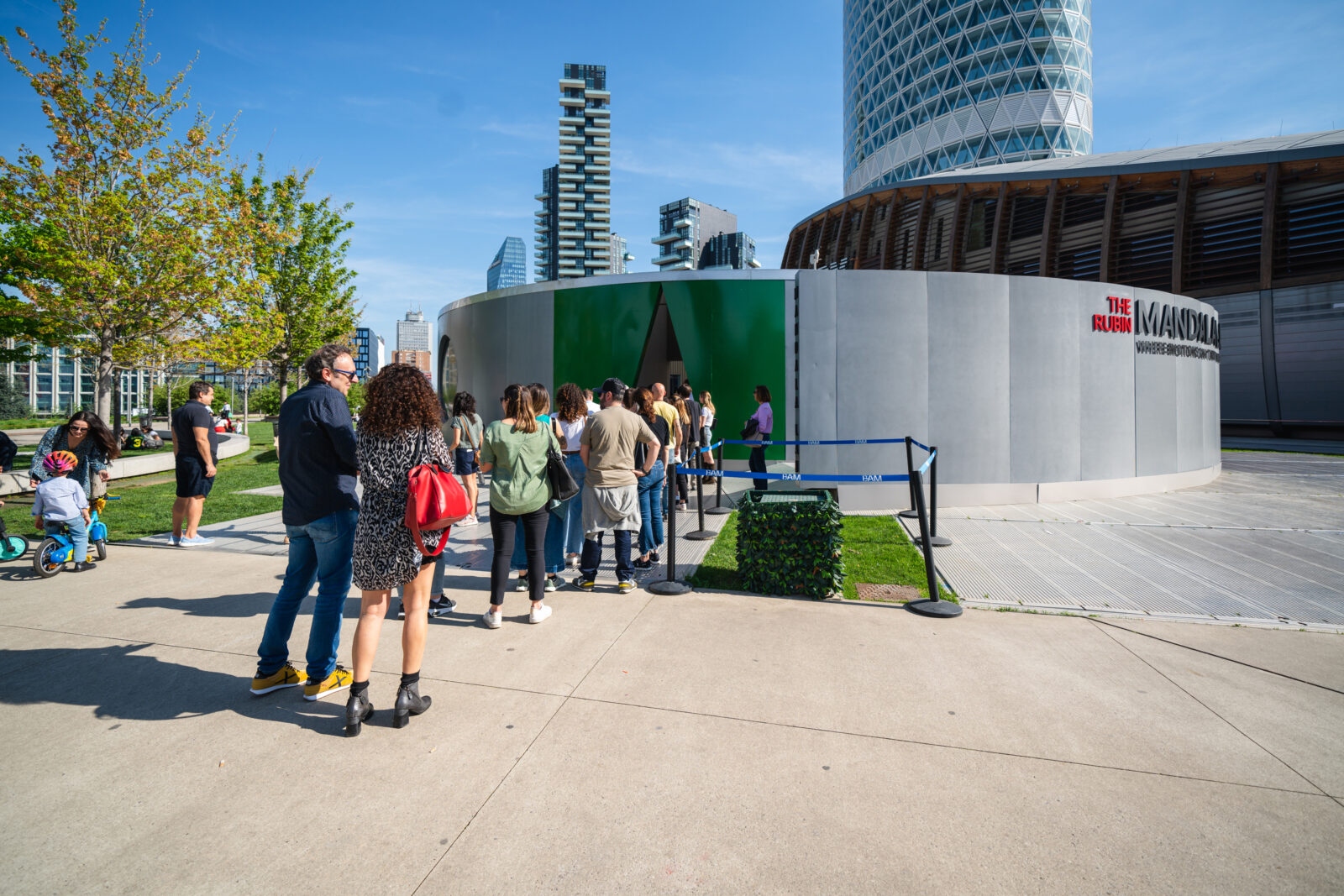 A line of people standing outside of the Mandala Lab installation structure with skyscrapers surrounding.