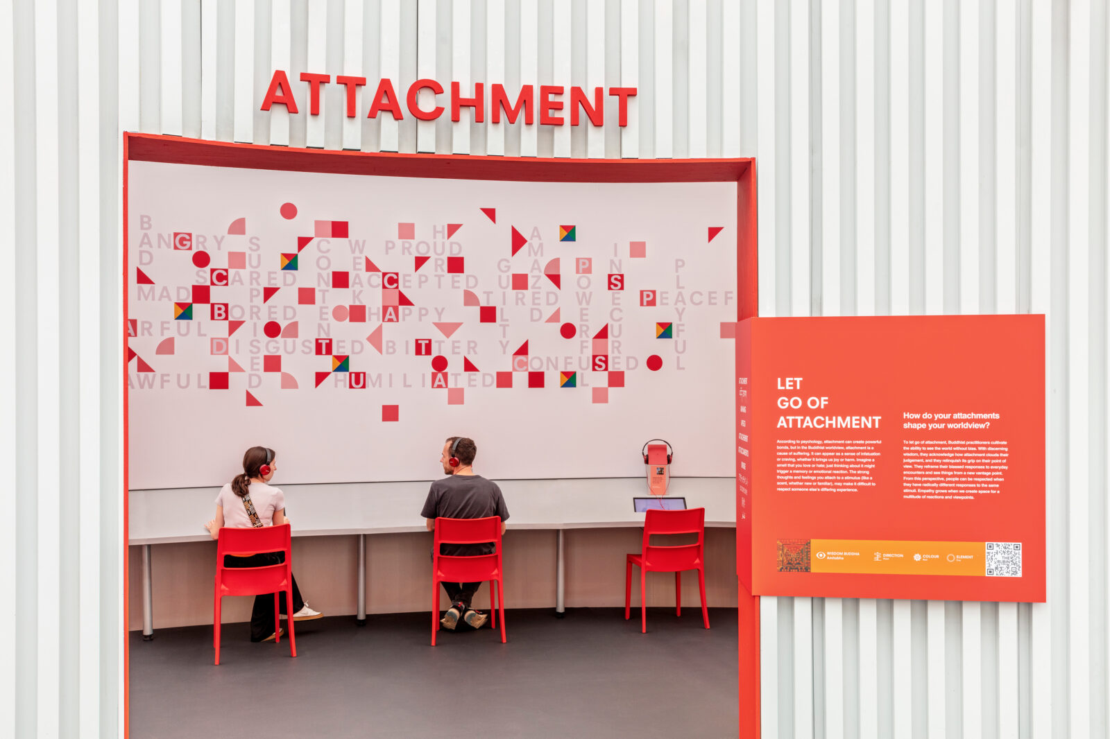 Open doorway with "Attachment" in red letters above. "Let go of attachment" in white text on red square on right side of opening. Two adults seated on red chairs beyond the opening.