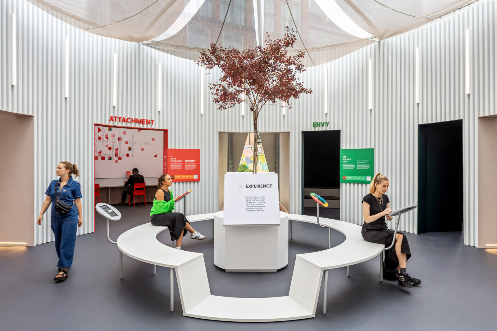 Interior of Mandala Lab installation with tree in center and people surrounding walking through the space and looking at interactive tablets.