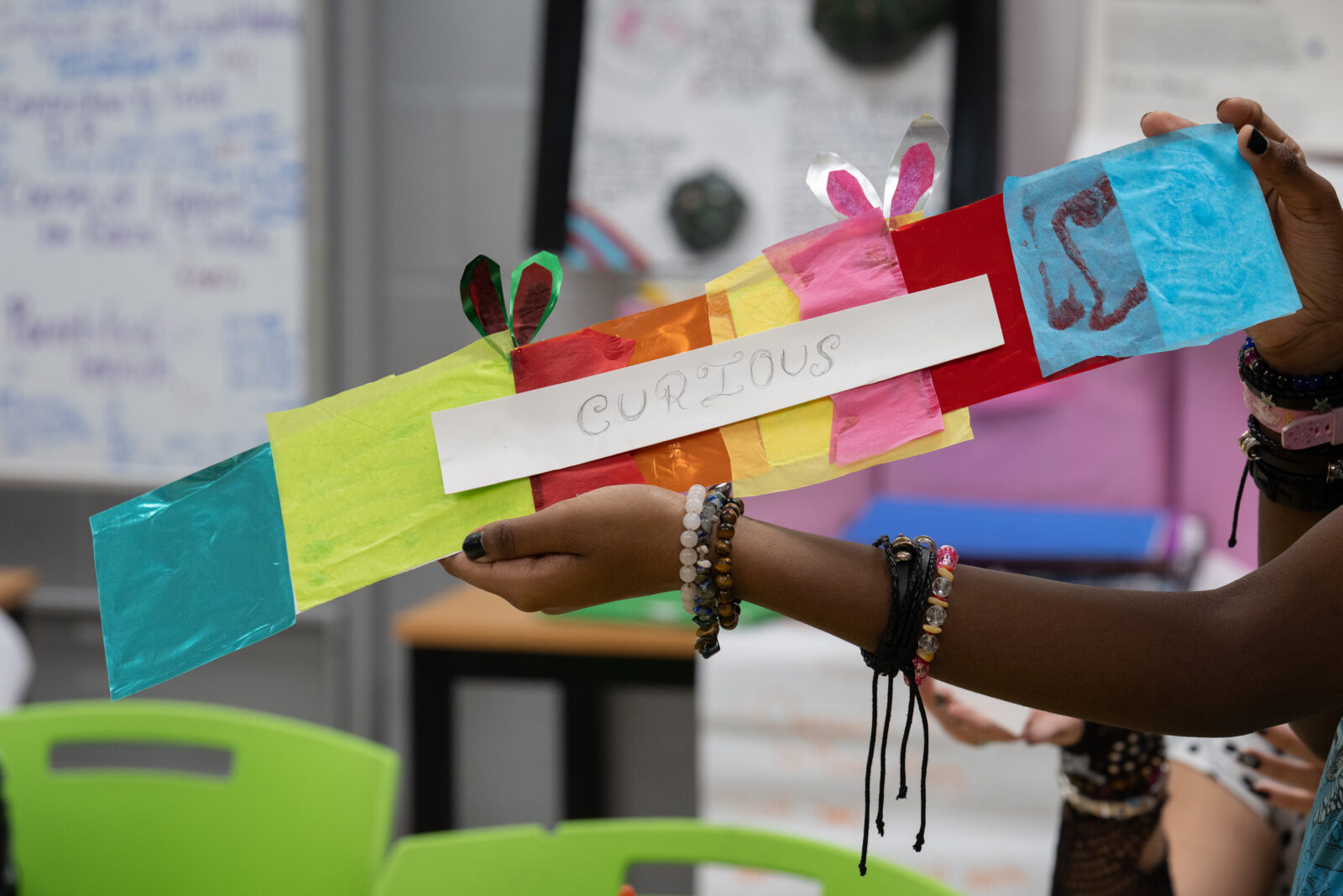student hands holding out an art project with the words "curiosity"